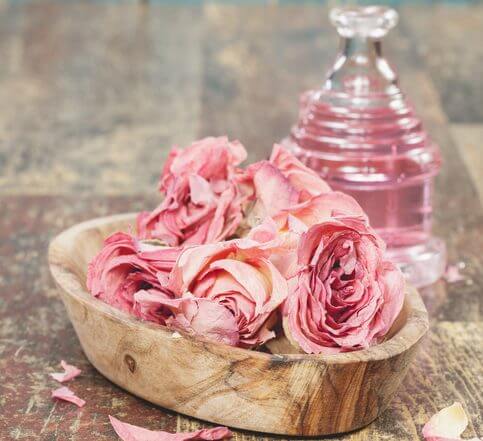 Essential oil with roses on rustic wooden background. A macro photograph with shallow depth of field. Done with a vintage retro filter